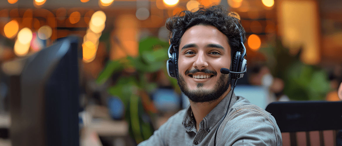 Customer service representative smiling and wearing a headset in a well-lit office environment. The Economic Advantages of Customer Service Outsourcing.